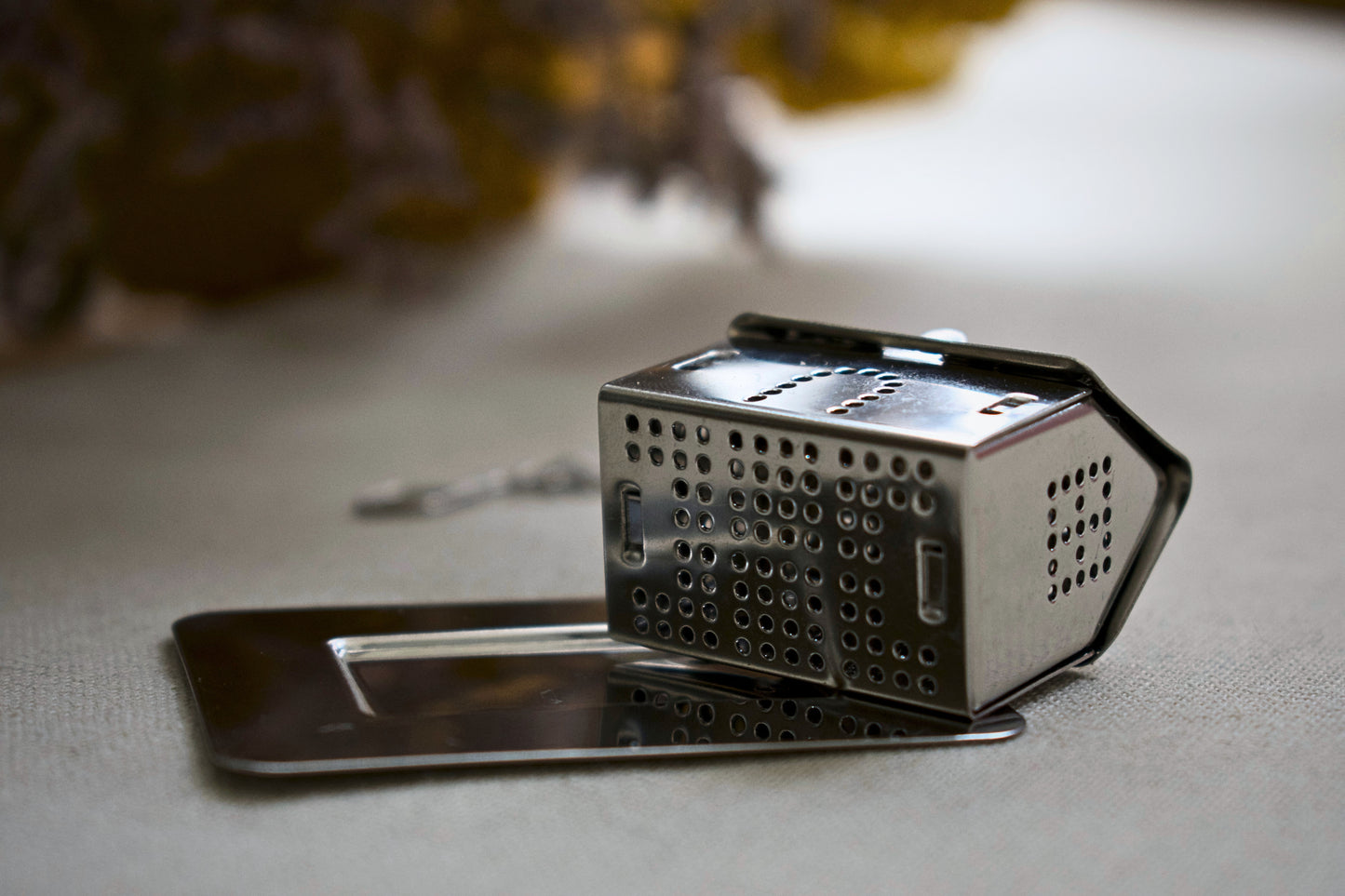 House shaped tea infuser lying on the side on a little stainless steel plate. The holed bottom is visible.