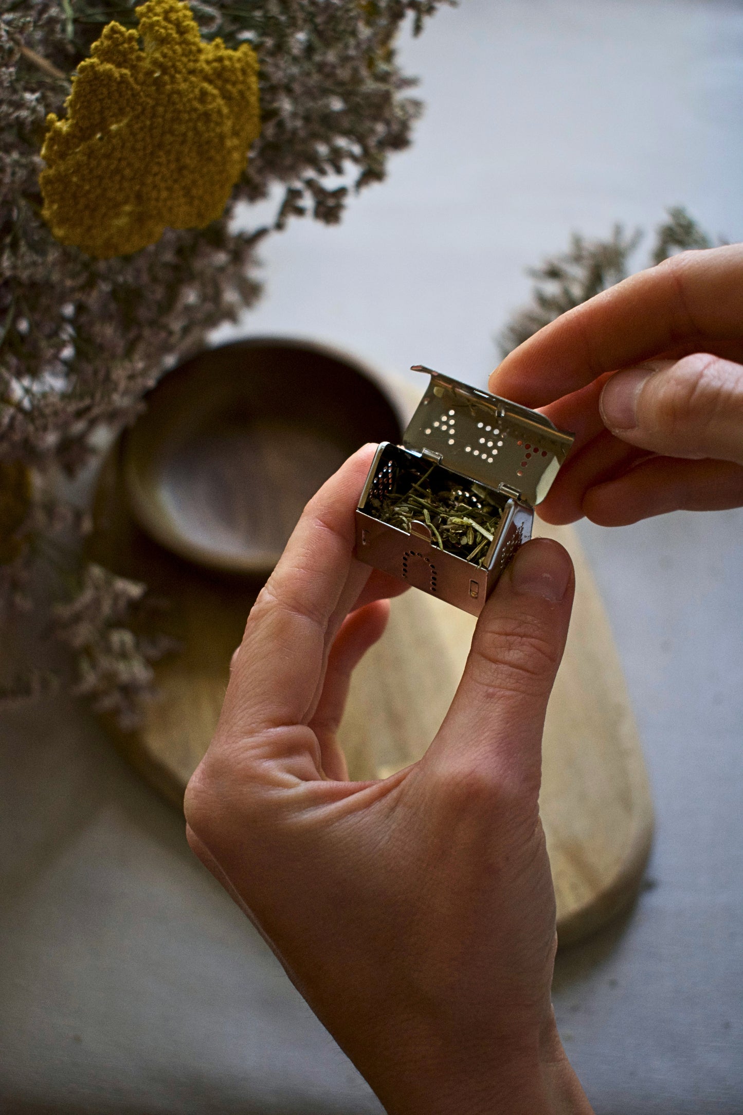 Person holding a tea house shaped strainer with some tea inside, against a natural background.