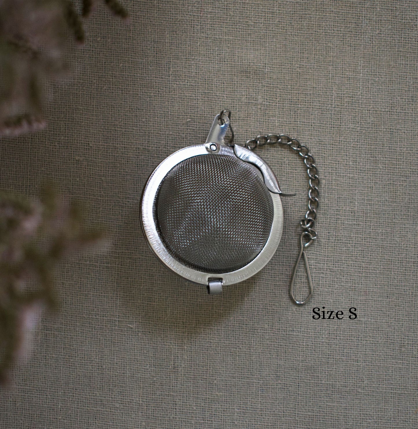 Round stainless steel size S tea infuser with chain on a linen tablecloth