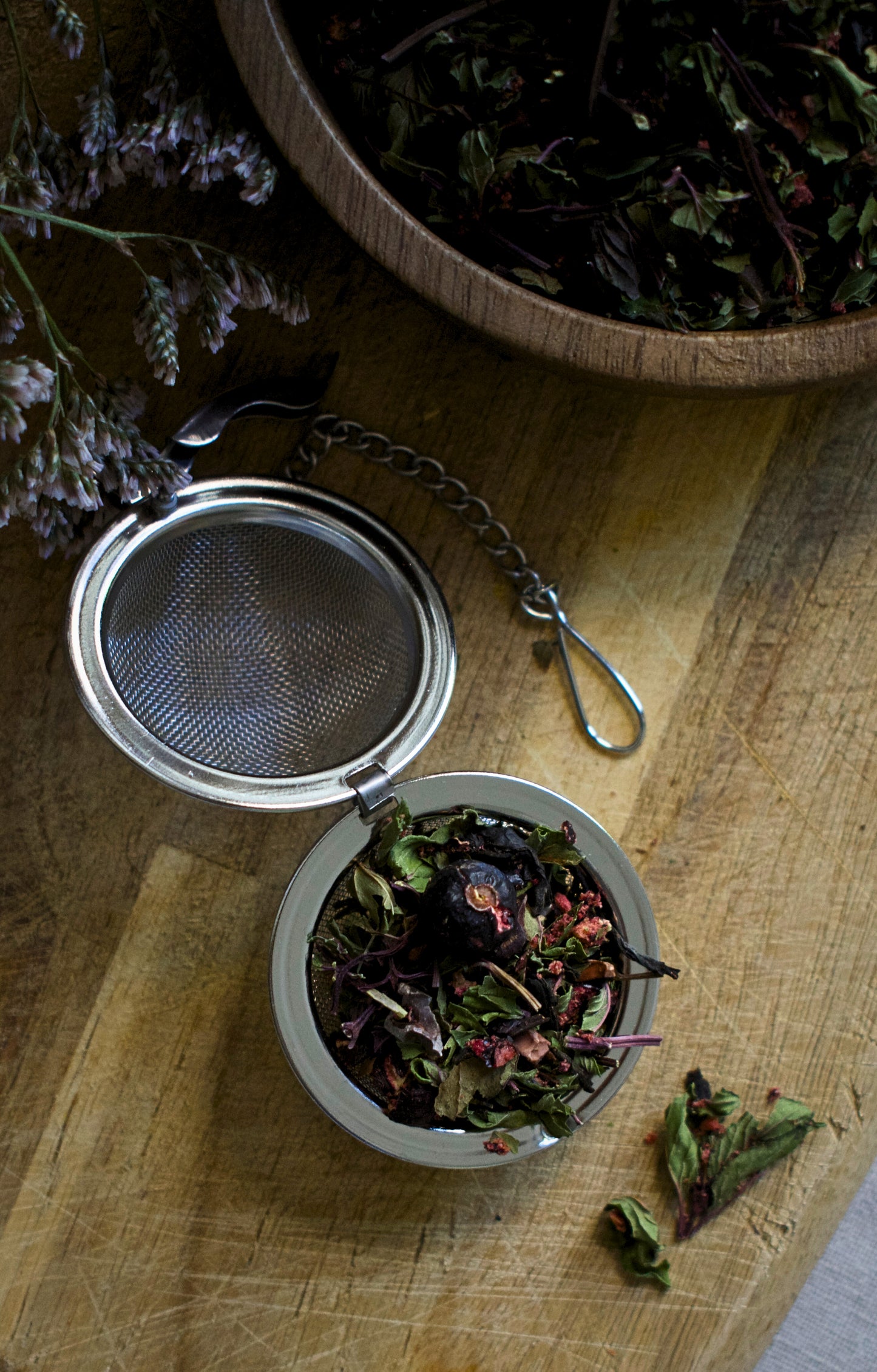 Smaller round tea strainer with dried herbs on a wooden surface