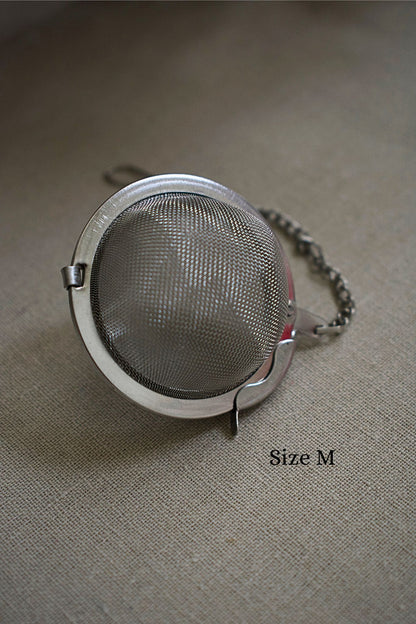 Metallic tea ball strainer on a textured surface with 'Size M' label.