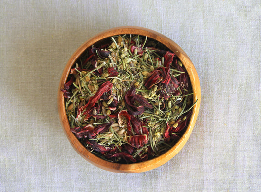 Herbal blend Happy Belly in a wooden bowl, allows us to  see all the ingredients; rosemary, hibiscus, fennel seeds, milk thistle and yarrow