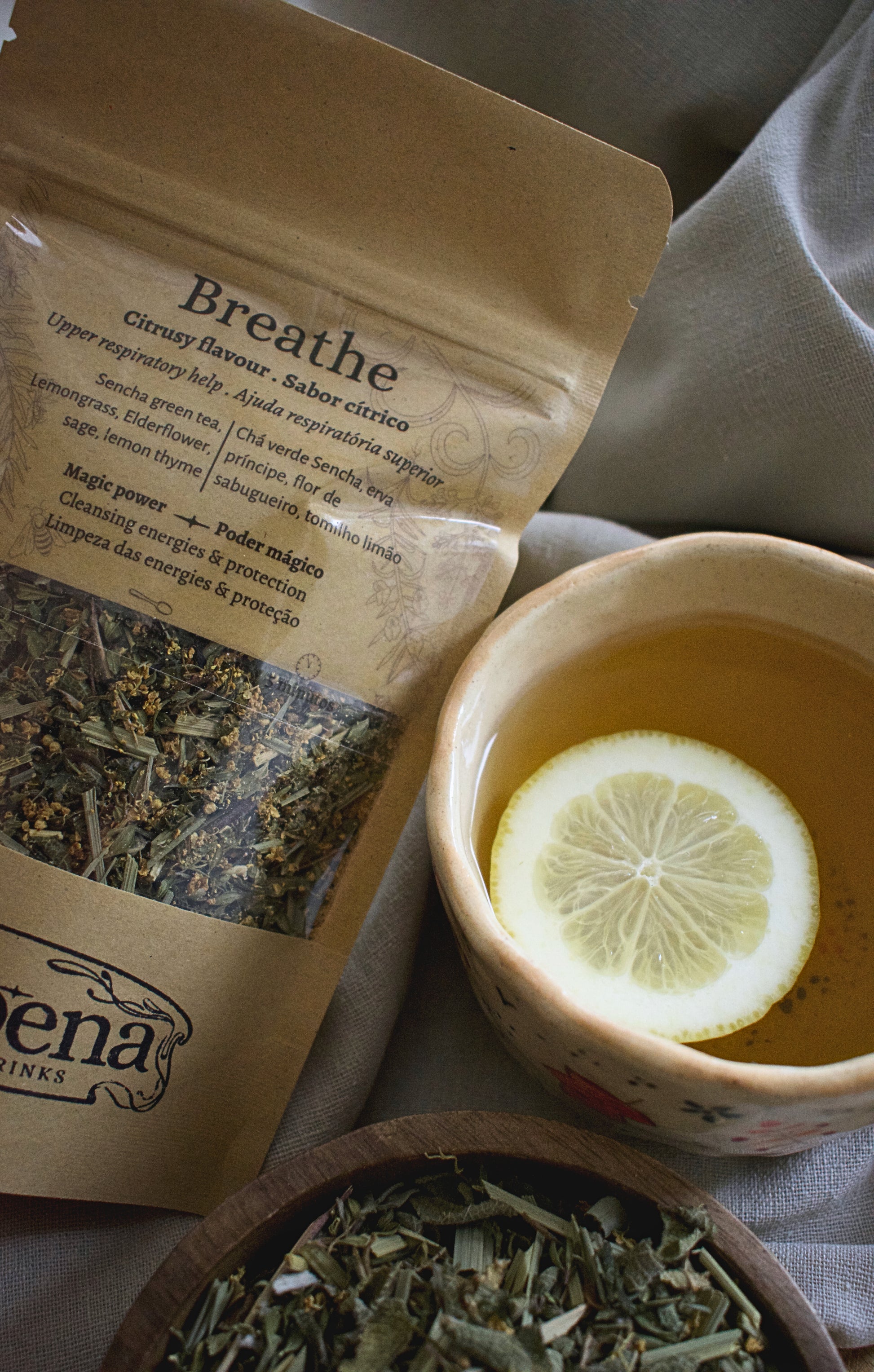 Tea blend Breathe in a kraft Bag besides a cup of tea with a lemon slide and a part of a wooden bowl with the breath tea blend.