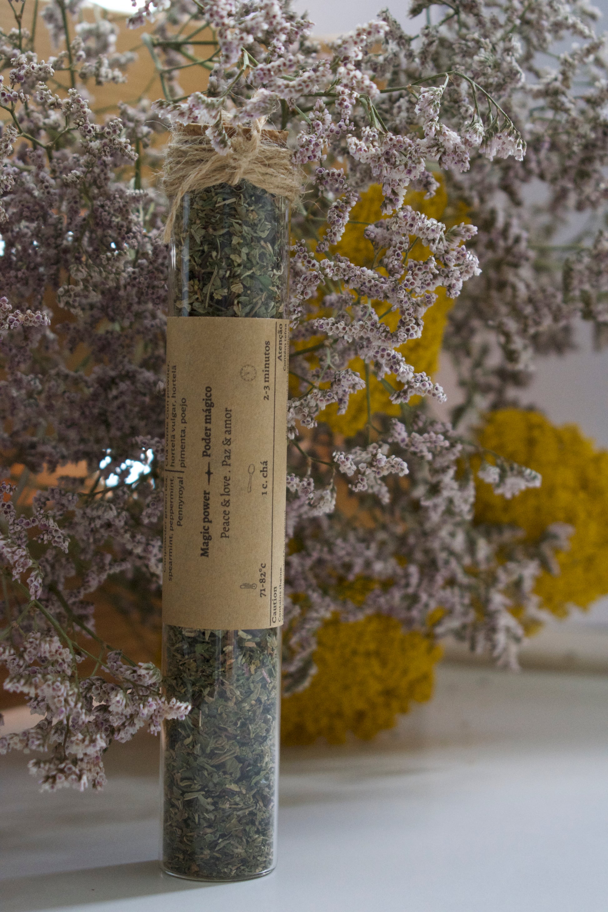 A glass tube with the tea blend Three Sisters standing up on a white surface, against a floral background