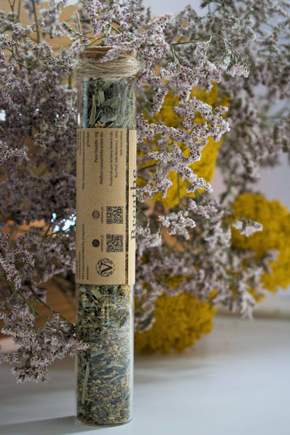 A glass tube with the tea blend Breathe standing up on a white surface, against a floral background