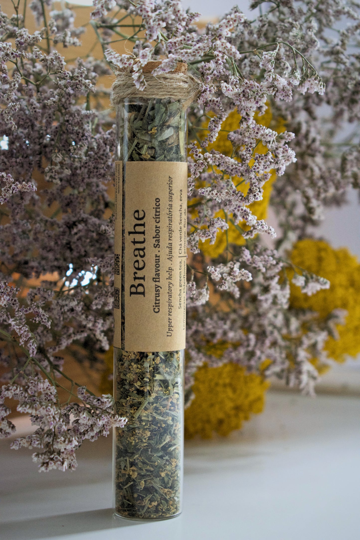A glass tube with the tea blend Breathe standing up on a white surface, against a floral background