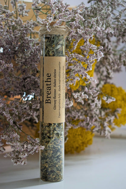 A glass tube with the tea blend Breathe standing up on a white surface, against a floral background