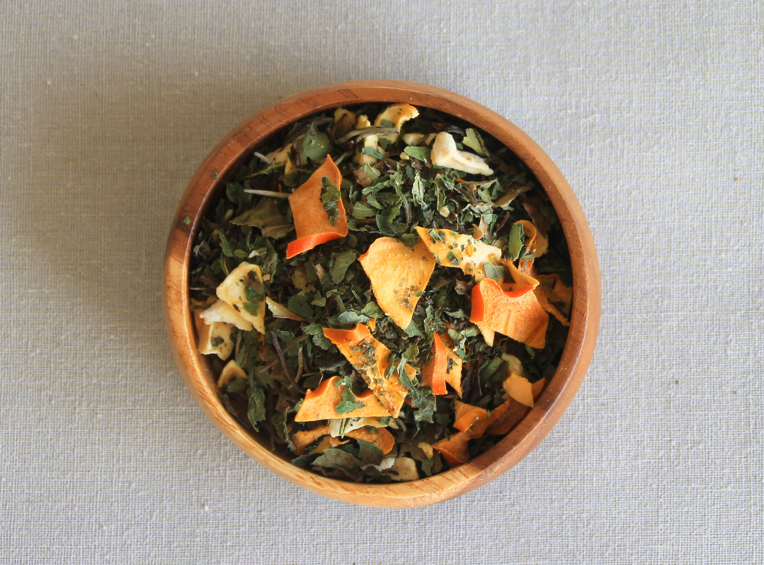 Herbal blend Luz Dulce in a wooden bowl, allows us to see all the ingredients; white tea, dried mango, dried persimmon, lemon balm