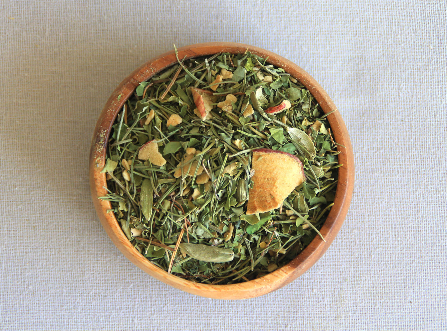 Herbal blend Mind Tonic in a wooden bowl, allows us to see all the ingredients; yerba mate, dried apple, rosemary, cardamome, moringa