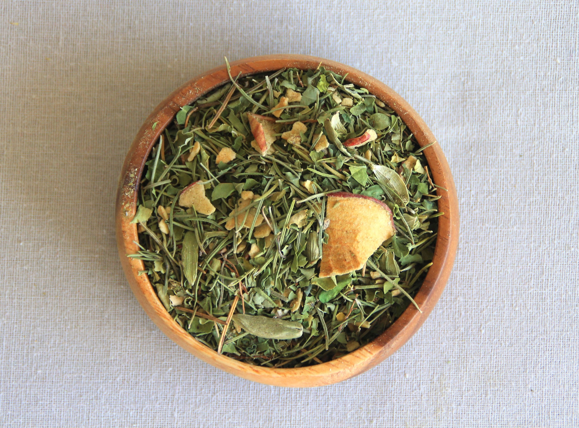 Herbal blend Mind Tonic in a wooden bowl, allows us to see all the ingredients; yerba mate, dried apple, rosemary, cardamome, moringa