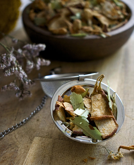 Round tea strainer with dried herbs on a wooden surface