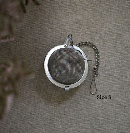 Round stainless steel size S tea infuser with chain on a linen tablecloth